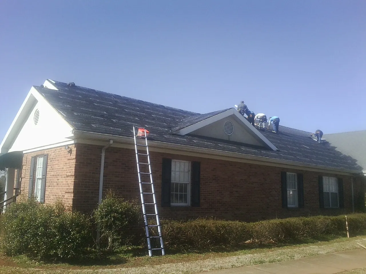 Crew tearing shingles off a brick ranch roof with a ladder set — Metal Roof Repair work by our crew in Marengo
