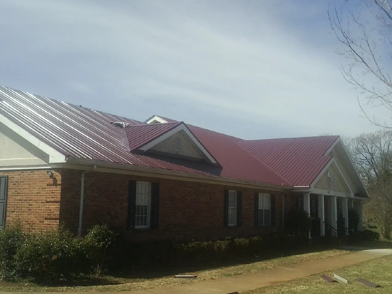 Red metal roof with gabled entries on a long brick building, from a Hail Damage Roof Repair job in Marengo