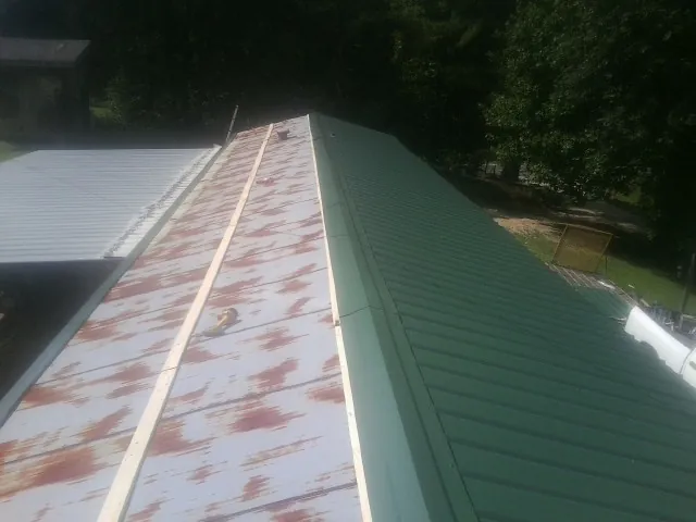 Old rusted panels beside newly installed green metal roofing — Wind Damage Roof Repair by Roofing Brothers in Marengo