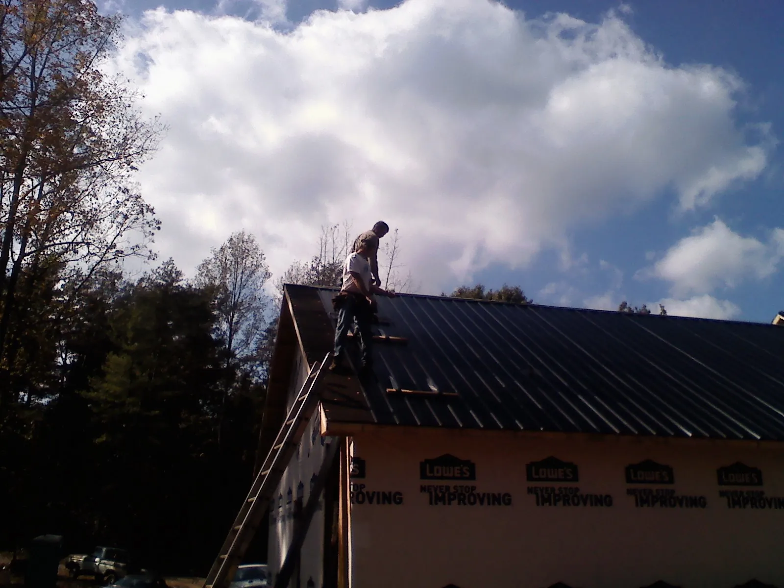 Roofer fastening dark metal panels high against a cloudy sky, from a Roof Inspection job in Marengo
