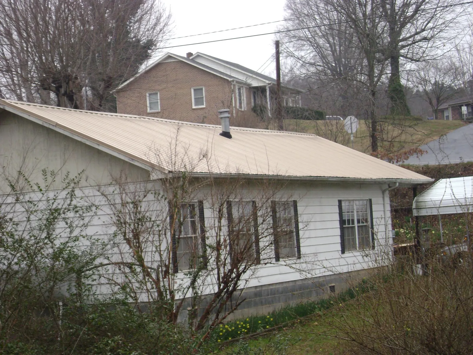 Tan metal roof on a white sided house set into a hillside — Commercial Roofing by Roofing Brothers in Marengo